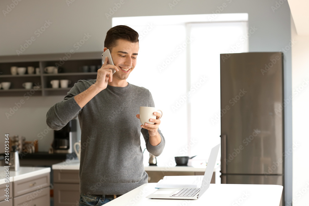 Young freelancer drinking coffee and talking on phone at home