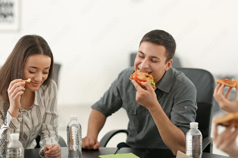 Young people eating pizza at table in office