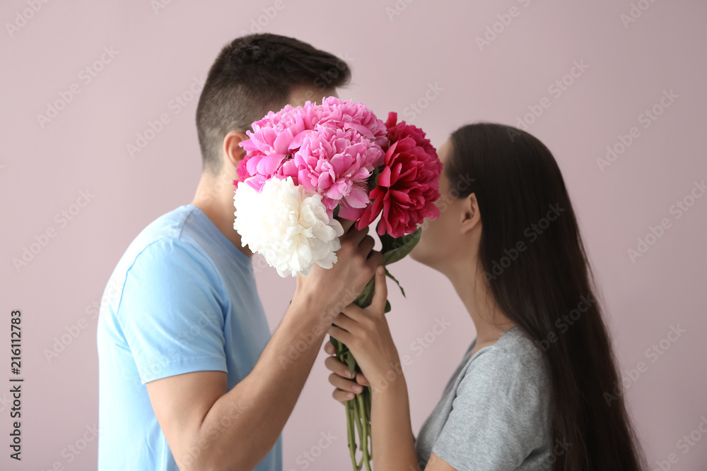 Happy young couple with flowers on color background