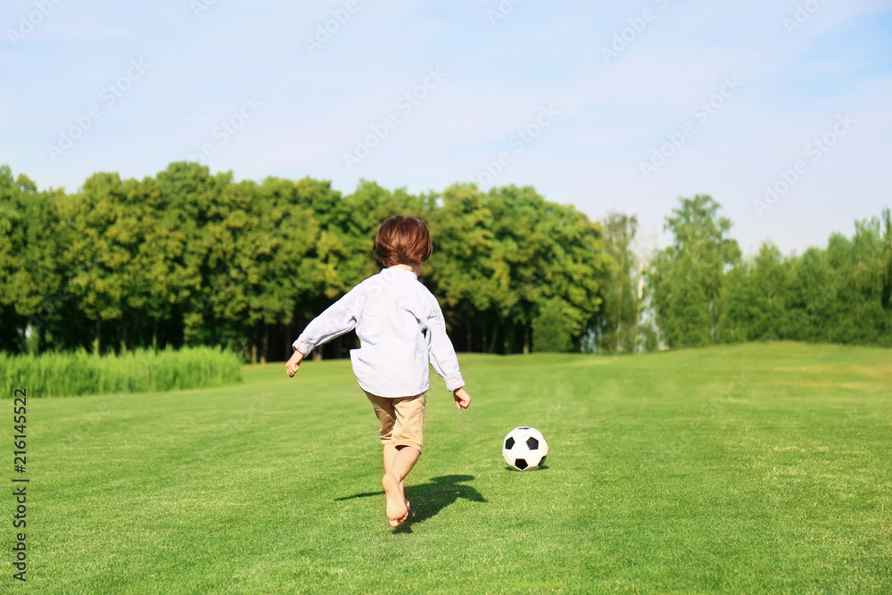 Cute little boy playing football in park on sunny day