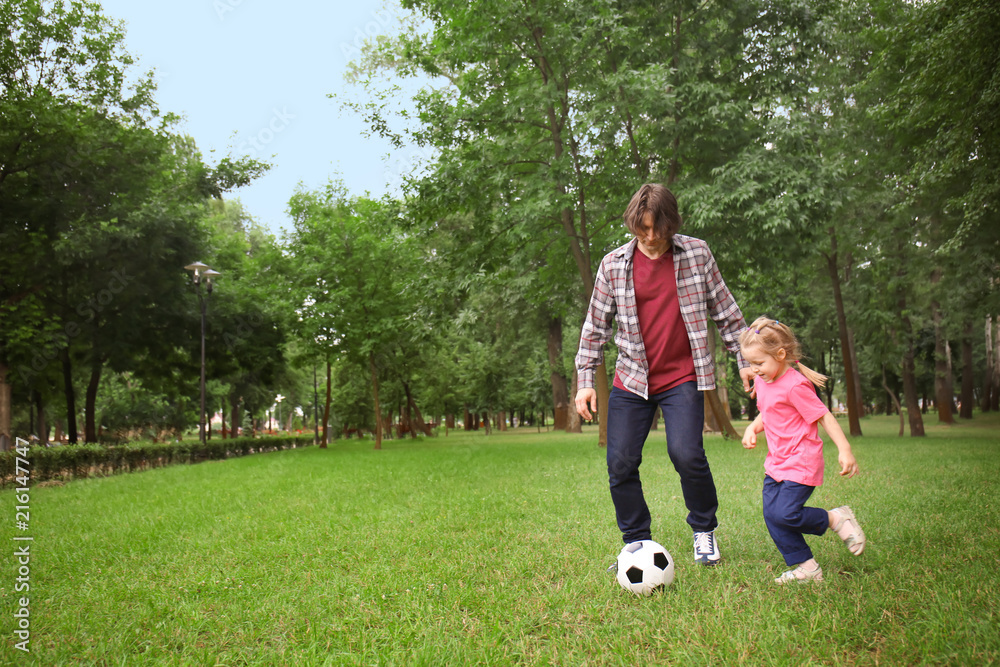 Happy father with daughter playing football in park on summer day