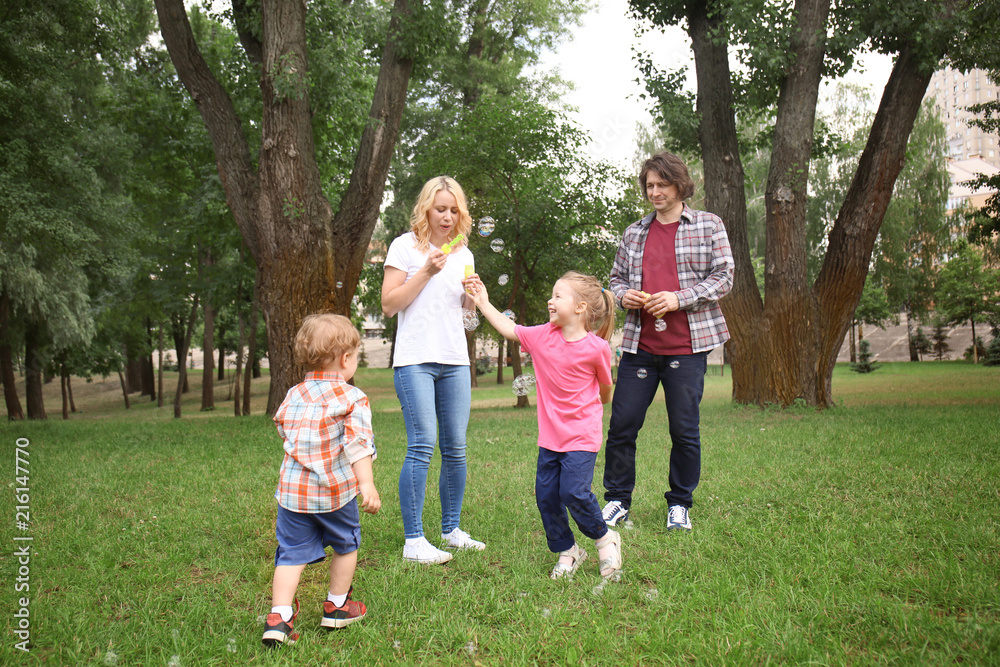 Happy family blowing soap bubbles in park