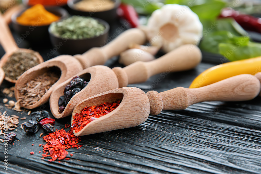 Scoops with different spices on wooden background