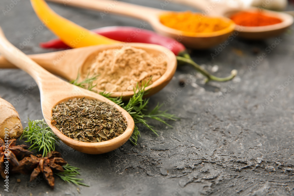 Wooden spoons with different spices on grey background