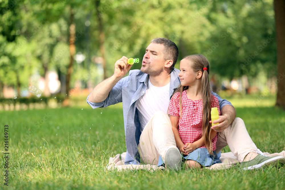 Happy father and daughter blowing soap bubbles in park