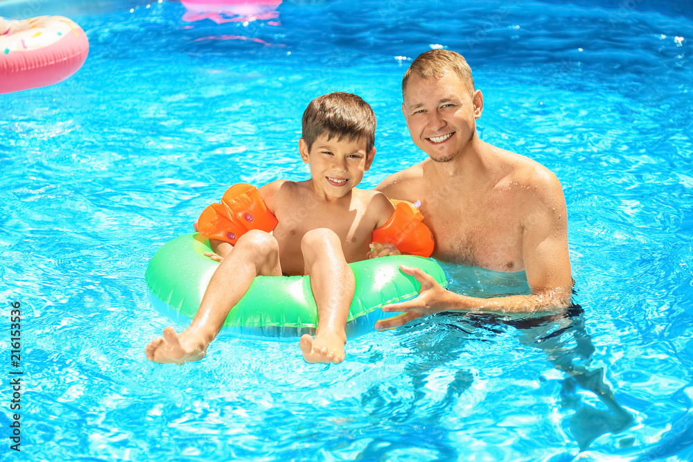 Happy father and son with inflatable ring in swimming pool