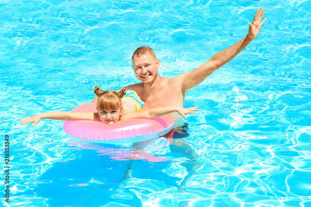 Happy father and daughter with inflatable ring in swimming pool