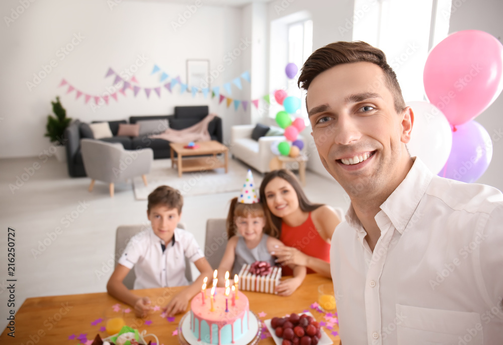 Young man taking selfie with family while celebrating daughters birthday at home