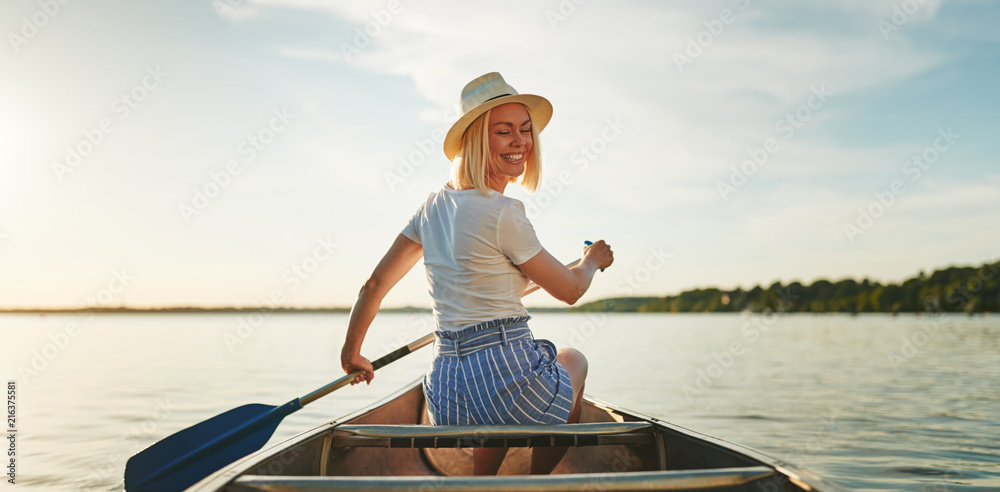 微笑的女人夏天在平静的湖面上划独木舟