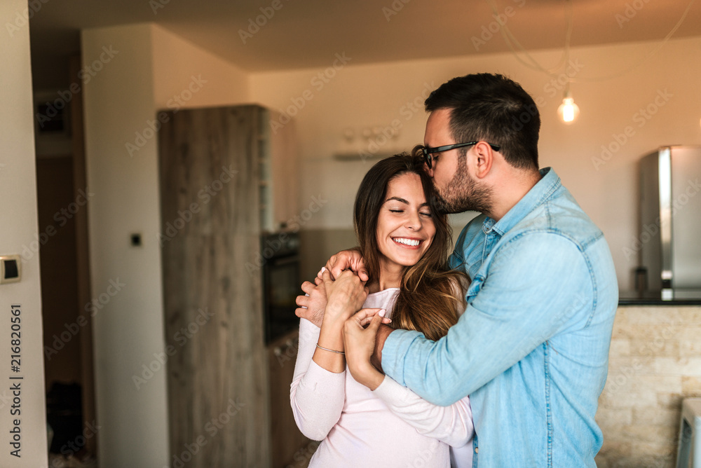 一名年轻男子在室内亲吻妻子的额头。