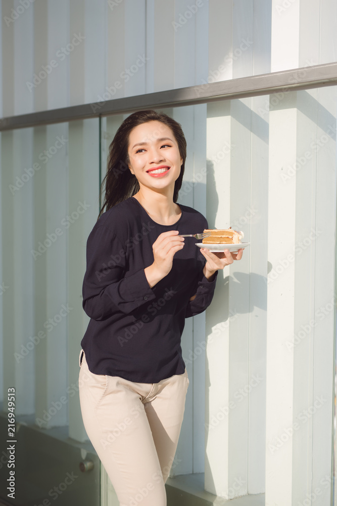 Young happy woman stands on the terrace of the hotel with dish cake in the morning. Pretty asian gir