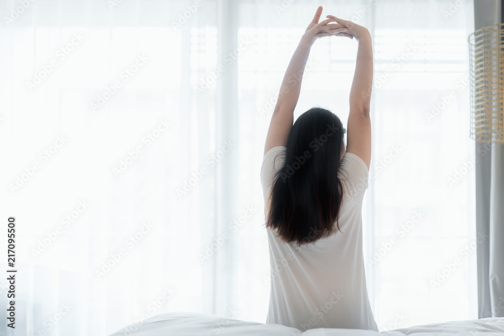 Asian Woman stretching in bed after wake up in bedroom at home, back view