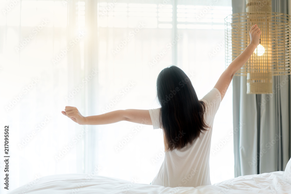 Asian Woman stretching in bed after wake up in bedroom at home, back view