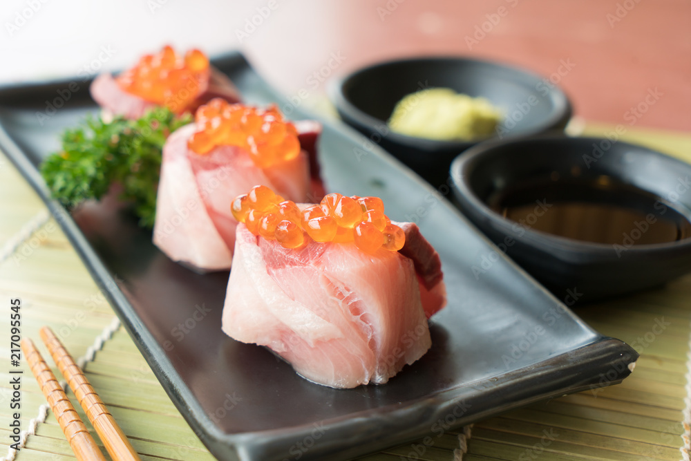 Salmon Roe on Hamachi sushi on black plate along with Japanese sauce and green leaf decoration, Japa