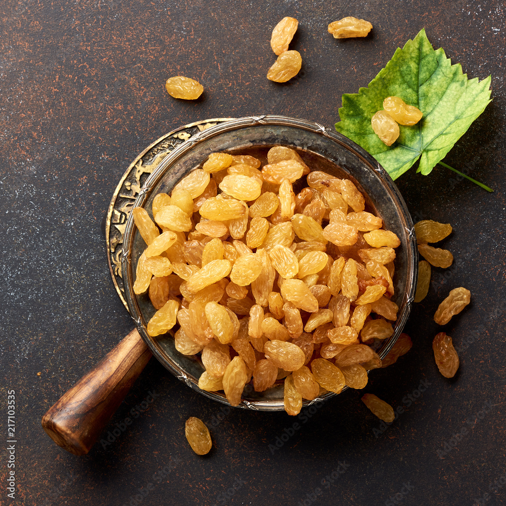 Heap of yellow raisins. Top view of dried grapes with green leaf.