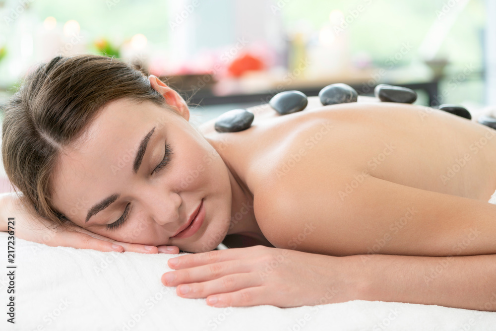 Hot stone massage treatment by therapist in spa.