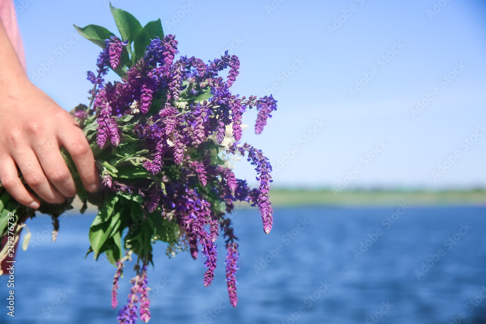 年轻女子在室外手持美丽的草地花朵，特写