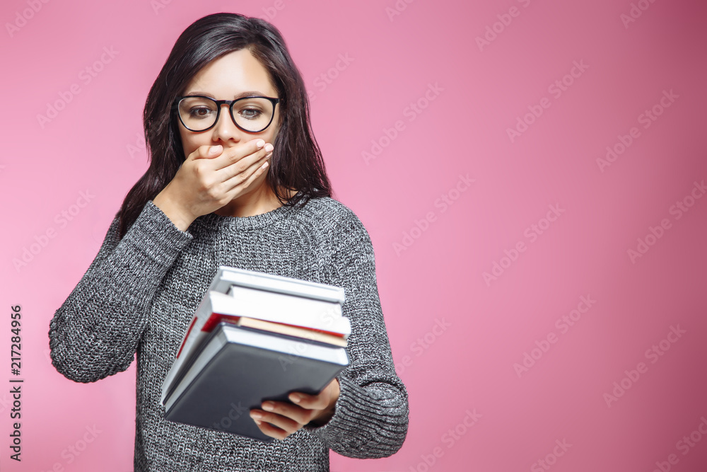 Portrait of scared girl student with books on pink background.