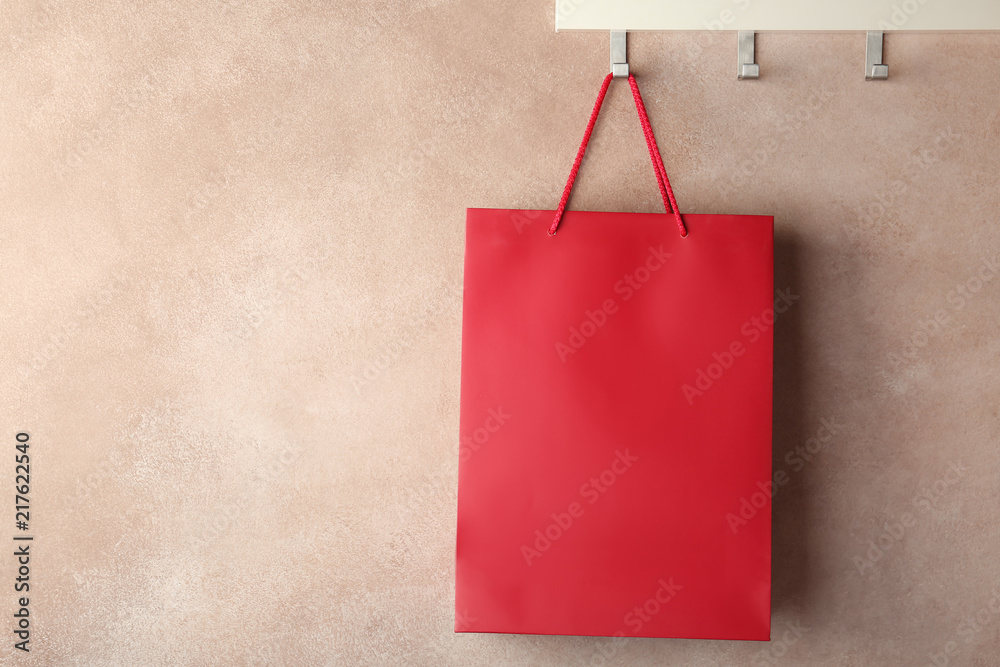 Rack with paper shopping bag on color wall. Mockup for design