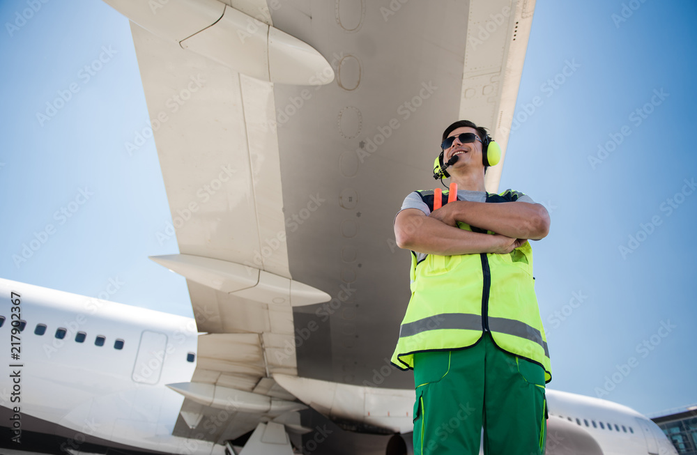 Enjoying sunny day. Low angle portrait of smiling man in sunglasses standing under airplane wing