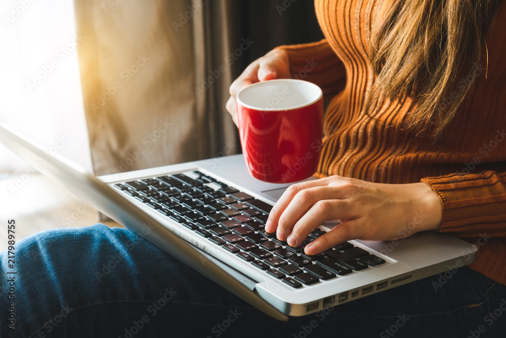 womman using laptop and typing and holding coffee cup in cafe, home office in morning light