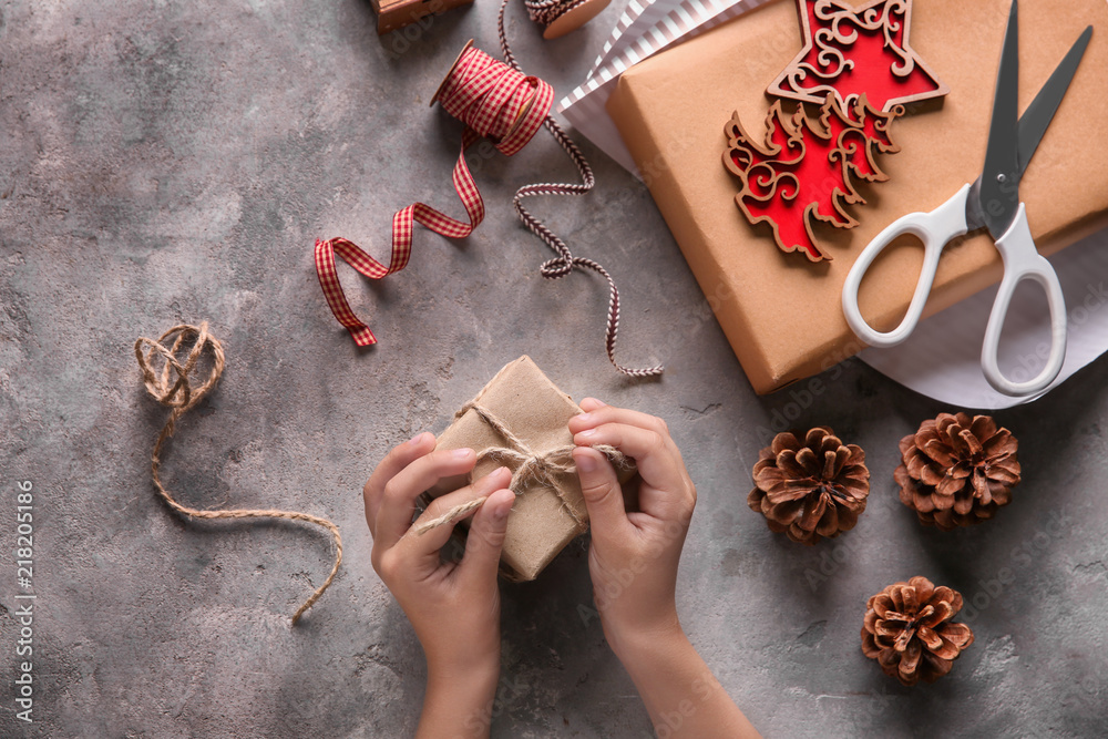 Child wrapping Christmas gift at table, top view