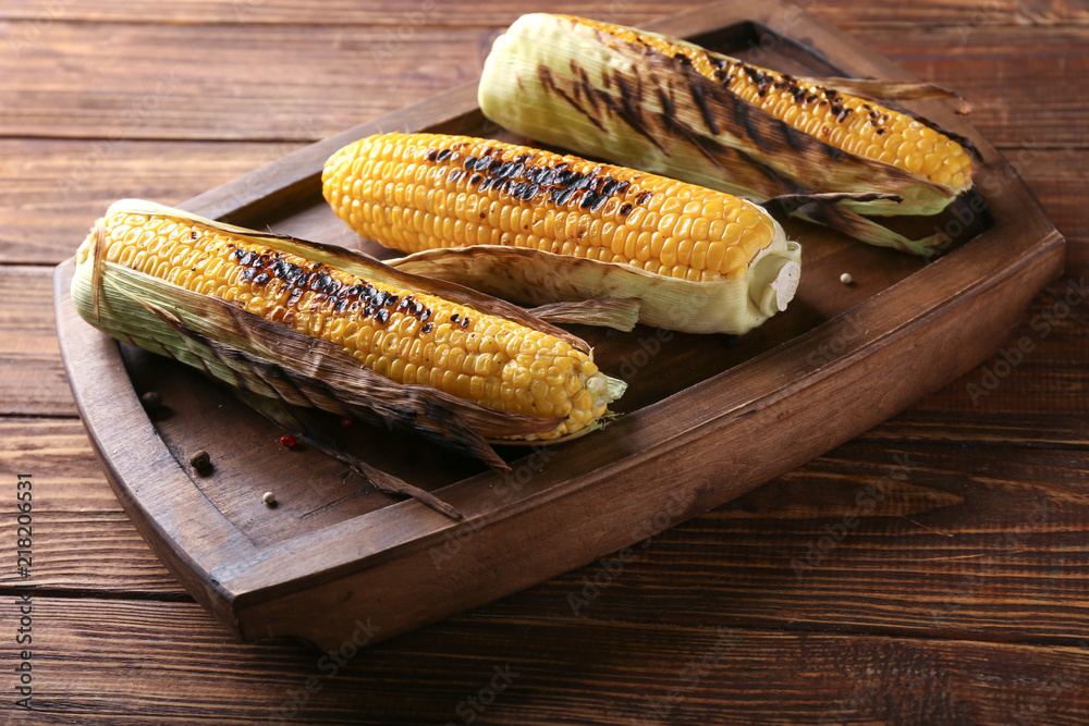 Wooden plate with delicious grilled corn on table