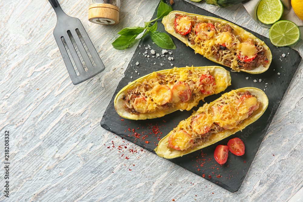 Slate plate with meat stuffed zucchini boats on wooden table