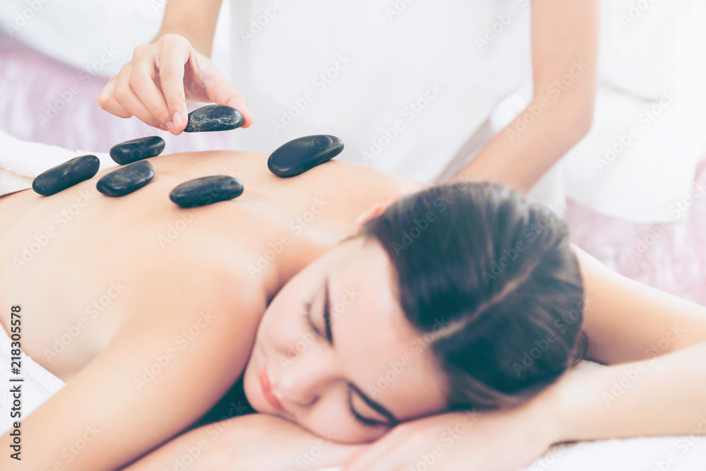 Hot stone massage treatment by therapist in spa.