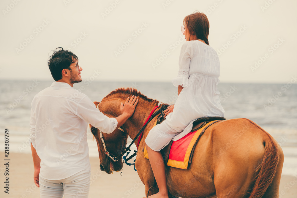 一对年轻夫妇在热带海滩上骑马。