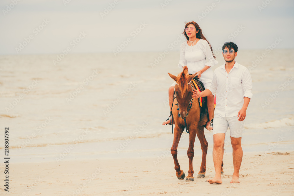 Young couple goes horse riding on tropical beach.