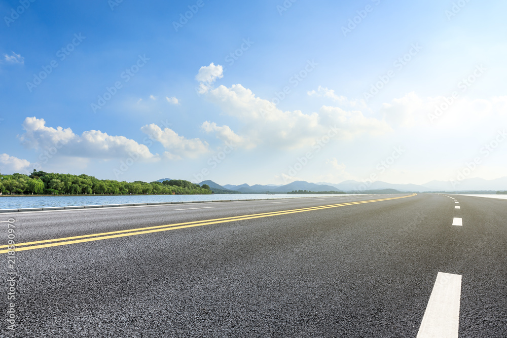 Empty asphalt road and lake with mountains on a sunny day