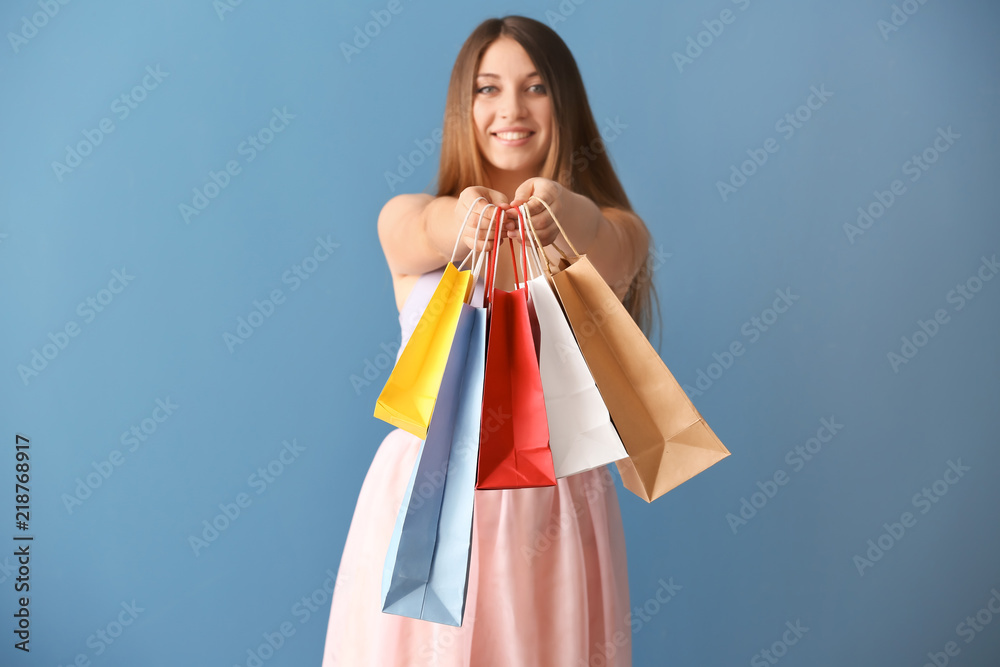 Beautiful young woman with shopping bags on color background