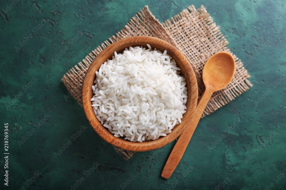 Wooden bowl with boiled white rice on color table