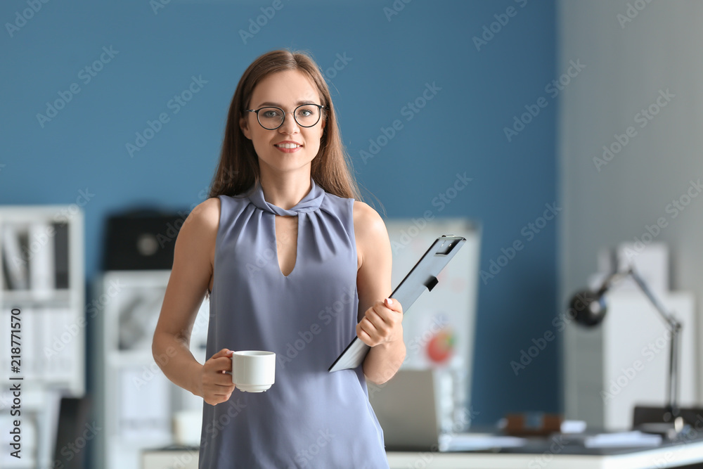 Young businesswoman with cup of coffee and clipboard in office