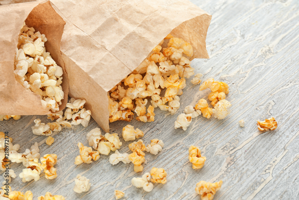 Paper bags with scattered delicious popcorn on wooden background, closeup