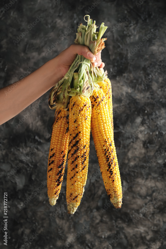 Woman holding grilled corn cobs on grey background