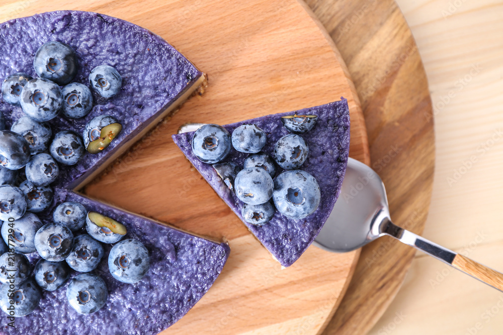 Taking of tasty blueberry cheesecake from board by using shovel