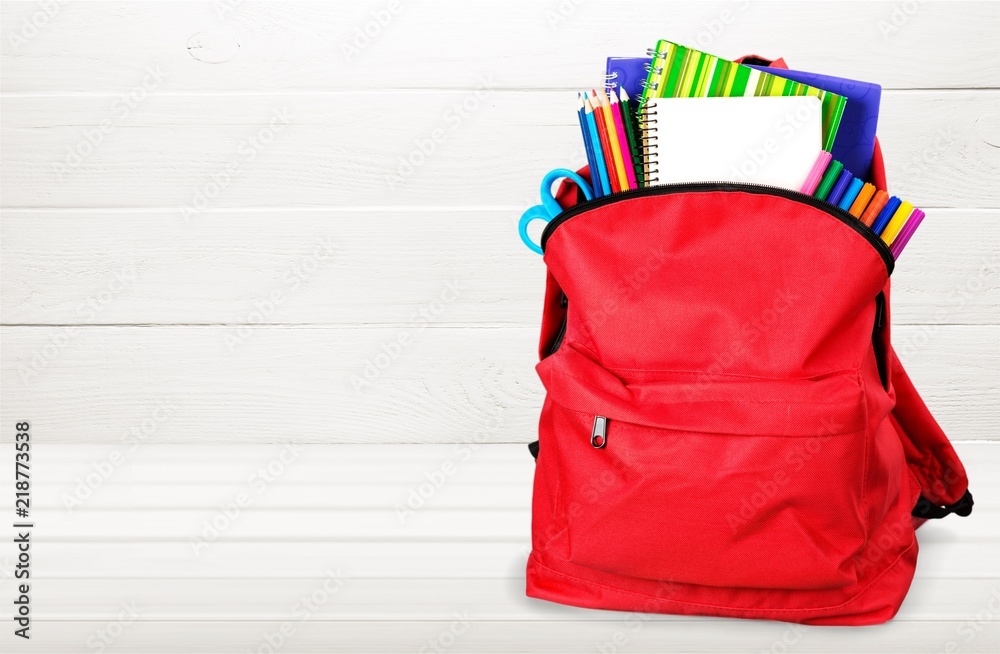 Colorful school supplies in backpack on wooden background