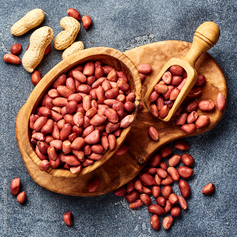 Peeled peanuts in bowl and scoop on gray background. Top view of nuts.