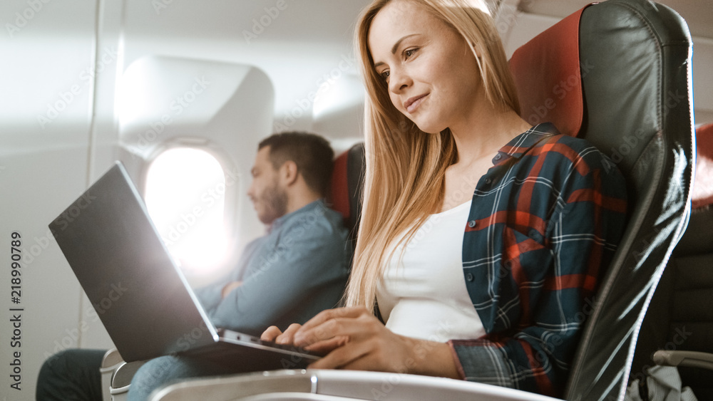 On Board of Commercial Airplane Beautiful Young Blonde Works on a Laptop while Her Hispanic Male Nei