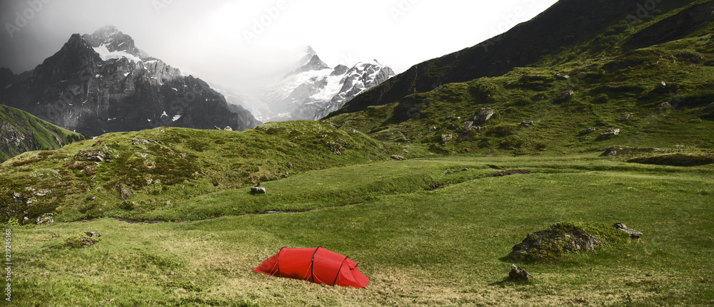 绿色和黄色草地上的红色帐篷，背景是高山。充满活力和戏剧性的天空，