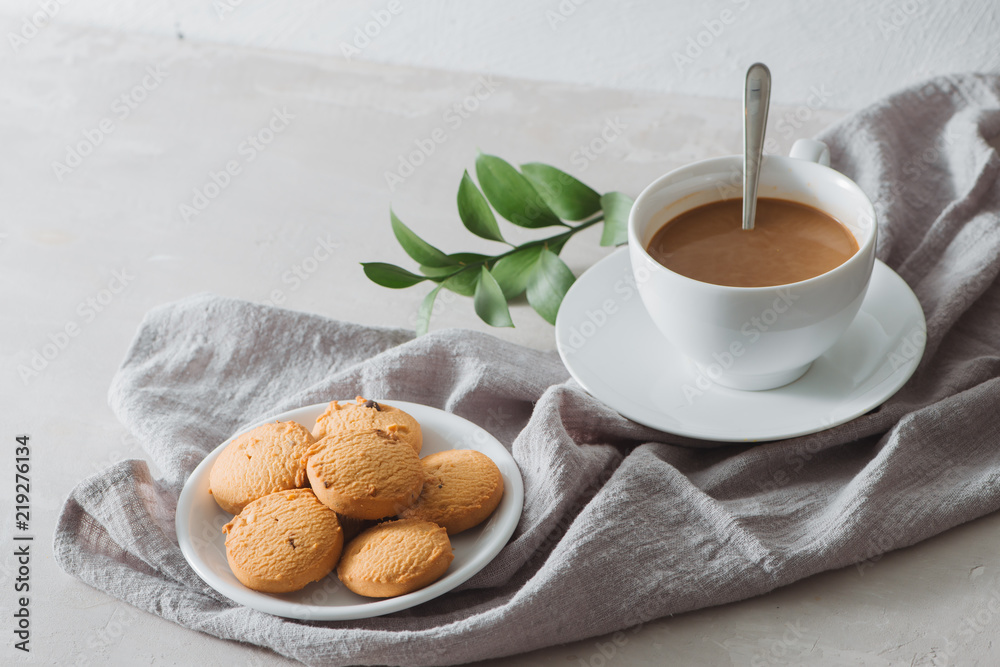 Closeup of coffee with milk in white cup and tasty cookies. Shot on light stone background