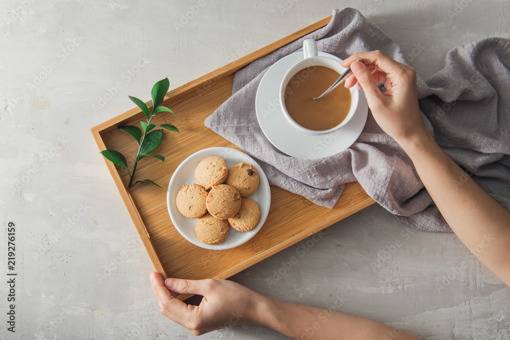 Male hands stir cup of coffee with milk and cookies on tray.