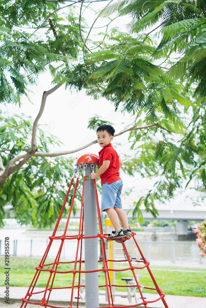 戴帽子的小男孩在公园的丛林健身房上攀爬