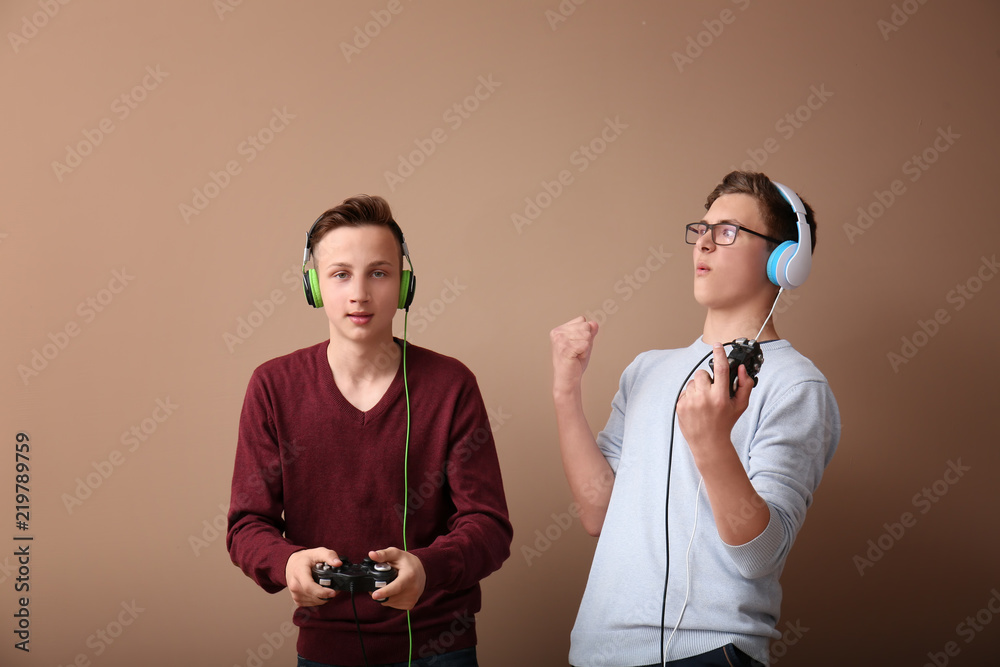 Teenagers with gamepads on color background