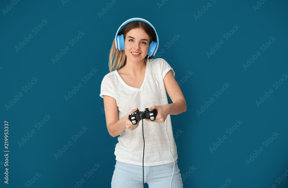 Young woman with gamepad on color background