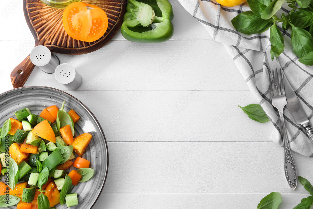 Plate with fresh vegetable salad and ingredients on white wooden table