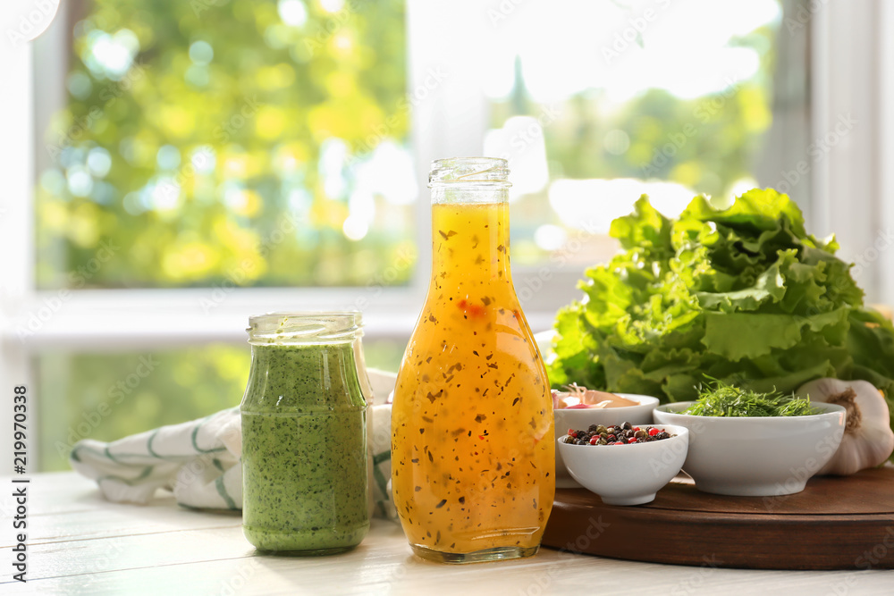 Bottle and jar with tasty sauces, spices and herbs on white wooden table