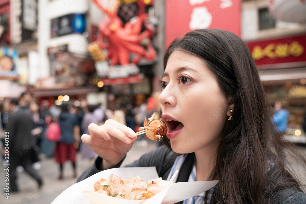 beautiful asian female eating takoyaki. view from side